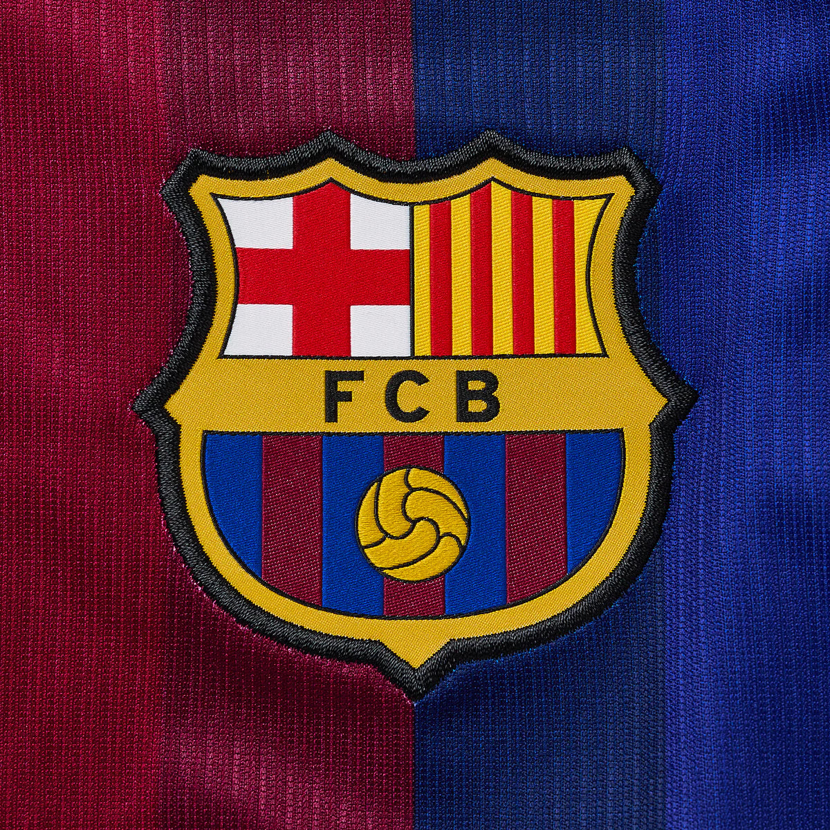 Close-up of an embroidered FC Barcelona crest patch centered on a textured red and blue striped fabric background.