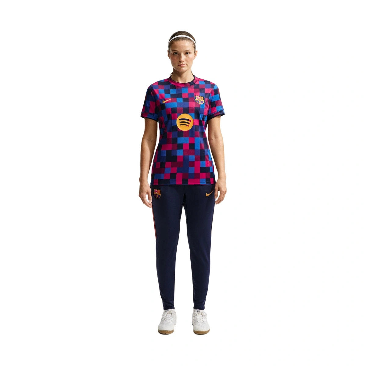 A woman modeling a short-sleeve FC Barcelona soccer jersey with a blue, red, and purple geometric pattern, paired with navy blue pants and white sneakers, on a solid white background.