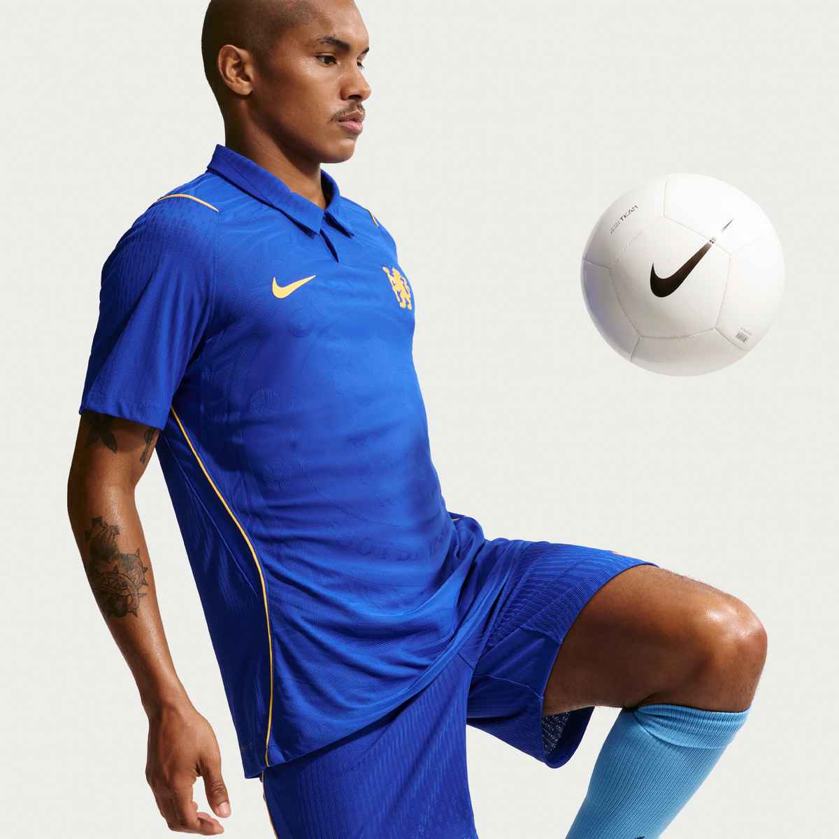 Man in blue sports outfit with Nike logo kicking a white soccer ball on a light gray background