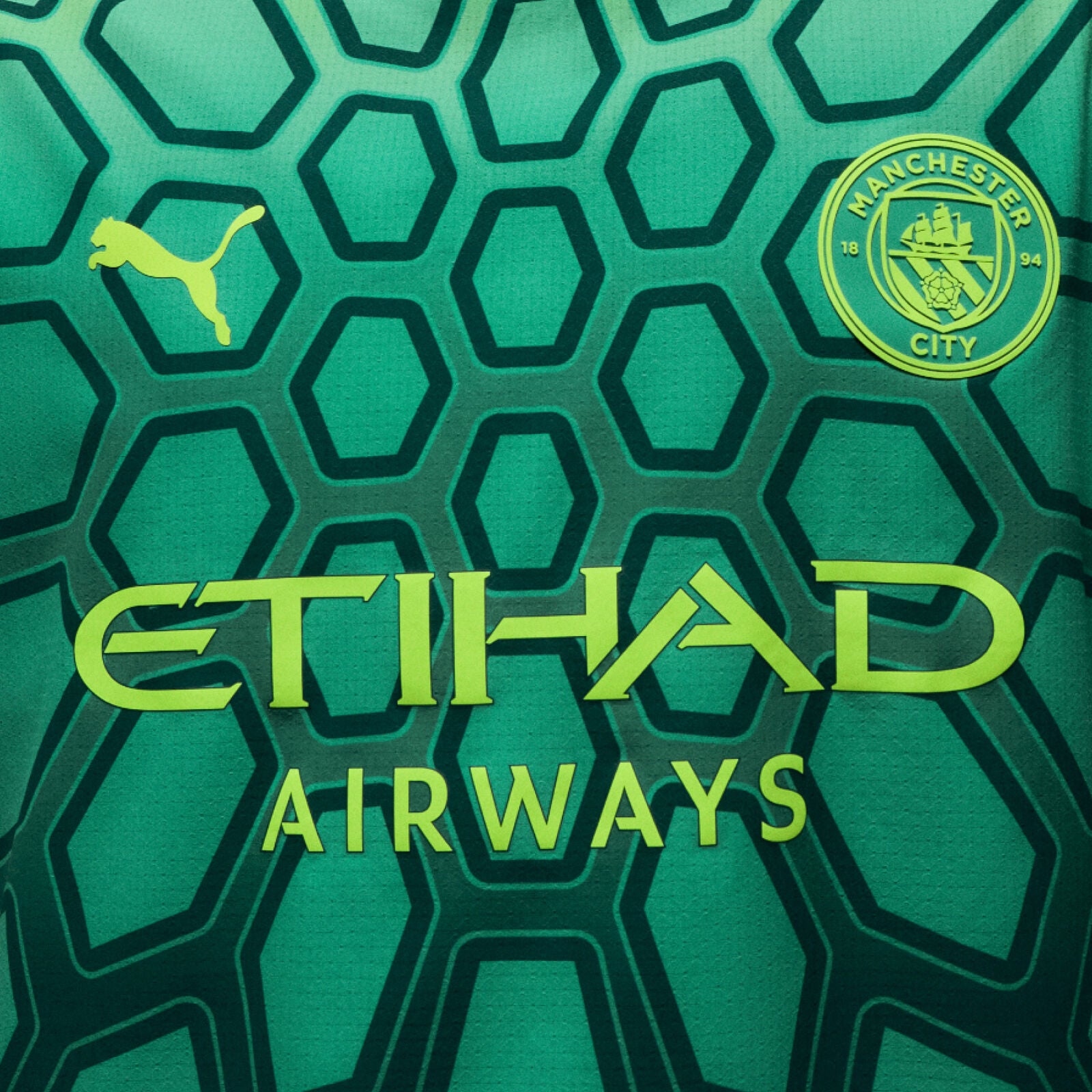 Green sports jersey with Puma logo, Manchester City emblem, and Etihad Airways text on a hexagonal pattern.
